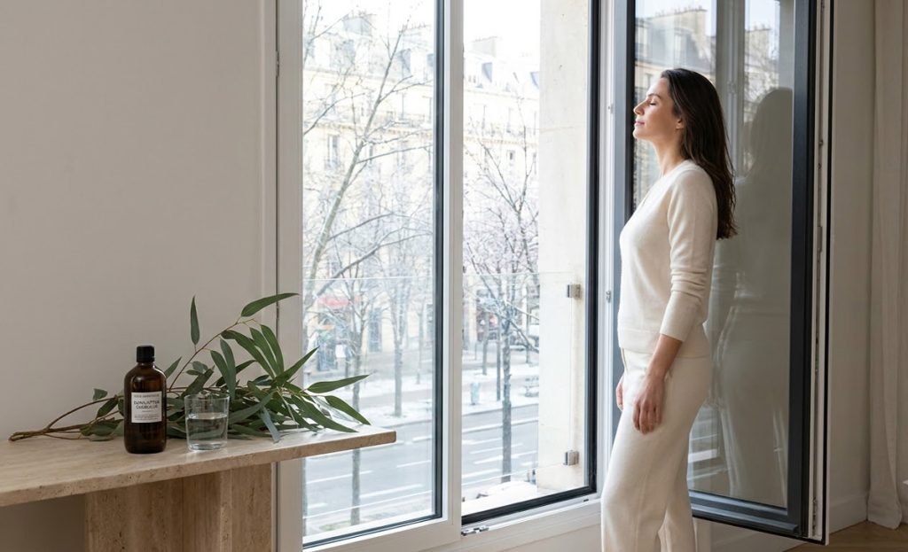 Huile essentielle eucalyptus : jeune femme respirant près d’une fenêtre avec Eucalyptus globulus